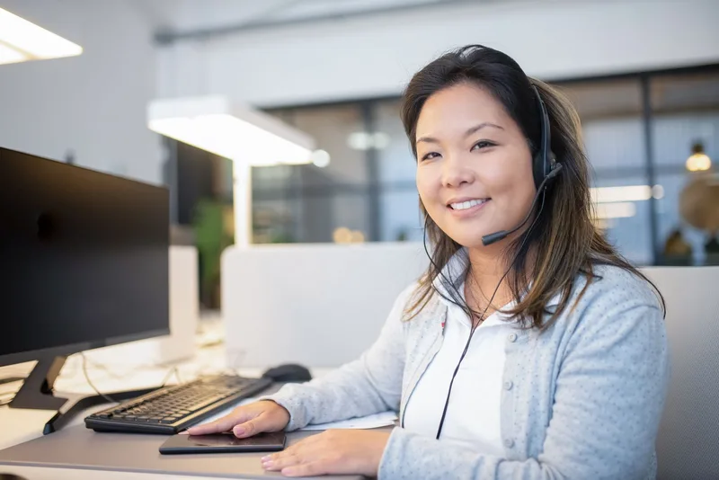 Smiling call center agent wearing a headset while working at her desk in a modern office setting