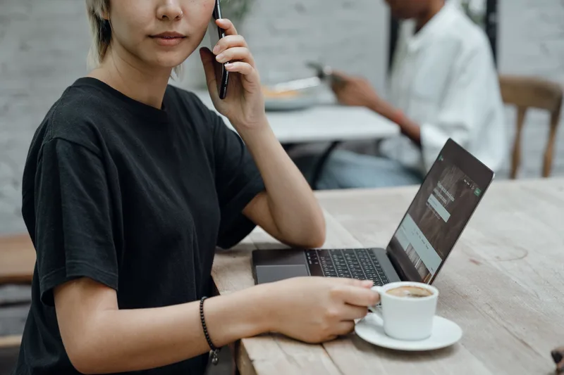 A freelancer checking messages on a phone next to a laptop, the kind of flexible setup many remote Amazon VA jobs allow