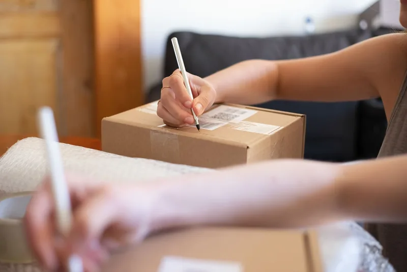 Hands labeling a shipping box, representing ecommerce store operations work