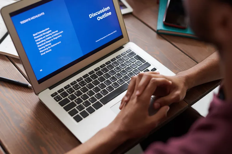 Person reviewing information on a laptop screen at a wooden desk