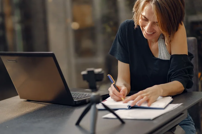Woman writing notes in a notebook next to an open laptop while learning a new skill at her desk