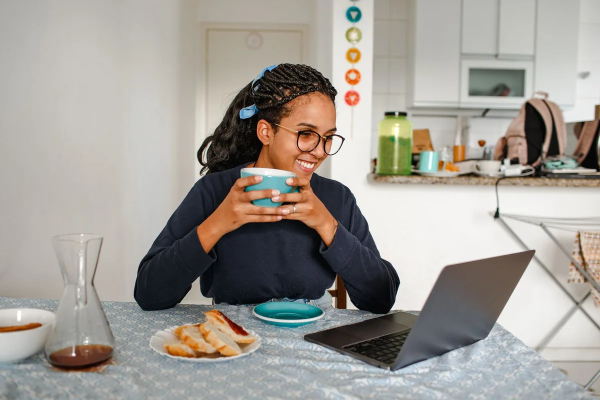 Remote worker smiling while working on a laptop with coffee at a home desk
