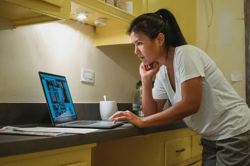 Filipino remote worker reviewing VA job listings on a laptop from a home kitchen