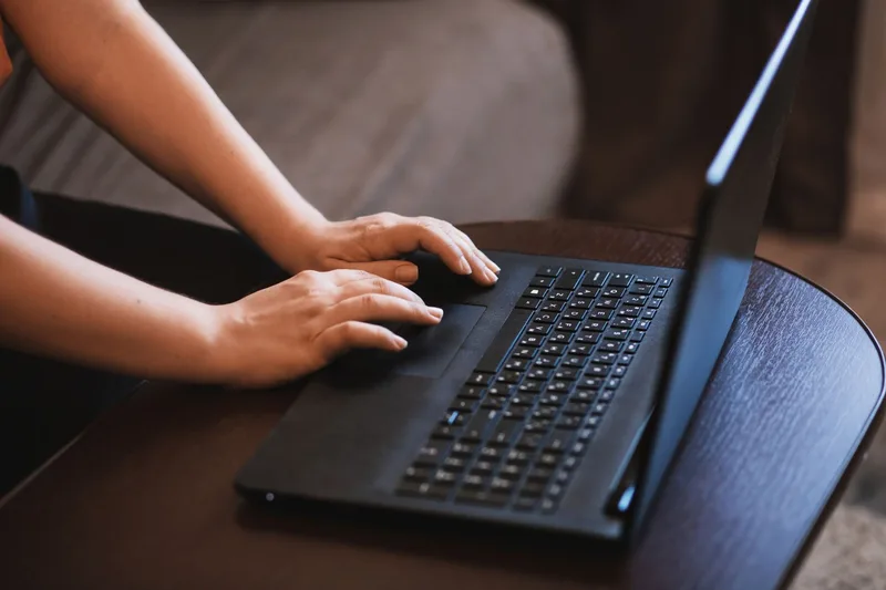 Close-up of hands typing on a laptop while searching for online virtual assistant job listings
